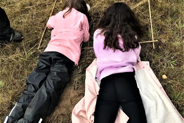 Fotografi på två barn som tittar på småkryp i en gräsmatta.