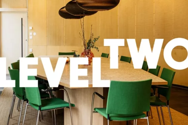 A room with a big wooden table and green chairs. On top of the picture it says Level Two in white letters. Photo.