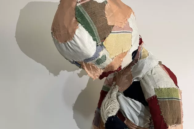 Ett konstverk föreställande en människa gjord av ihopsydda tygbitar i olika färger. Foto.