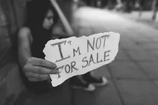 En person sitter på gatan och håller upp en skylt där det står I'm not for sale. Foto.