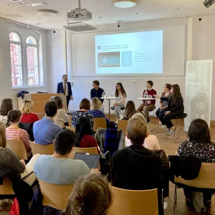 Personer pratar inför en sittande publik på Pufendorfinstiutetet. Foto.